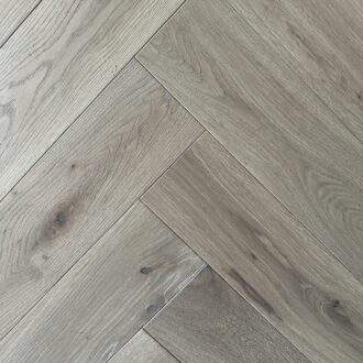 Light smoked brushed hardwood boards form a herringbone pattern, with pale grain and subtle knots creating a calm, natural wood surface.