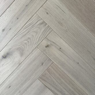 Light natural-washed herringbone wood flooring shows pale oak planks with subtle knots and grain laid in a crisp diagonal pattern across the surface.