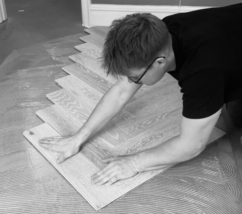 An installer presses light wood flooring boards into adhesive while fitting a residential floor indoors.